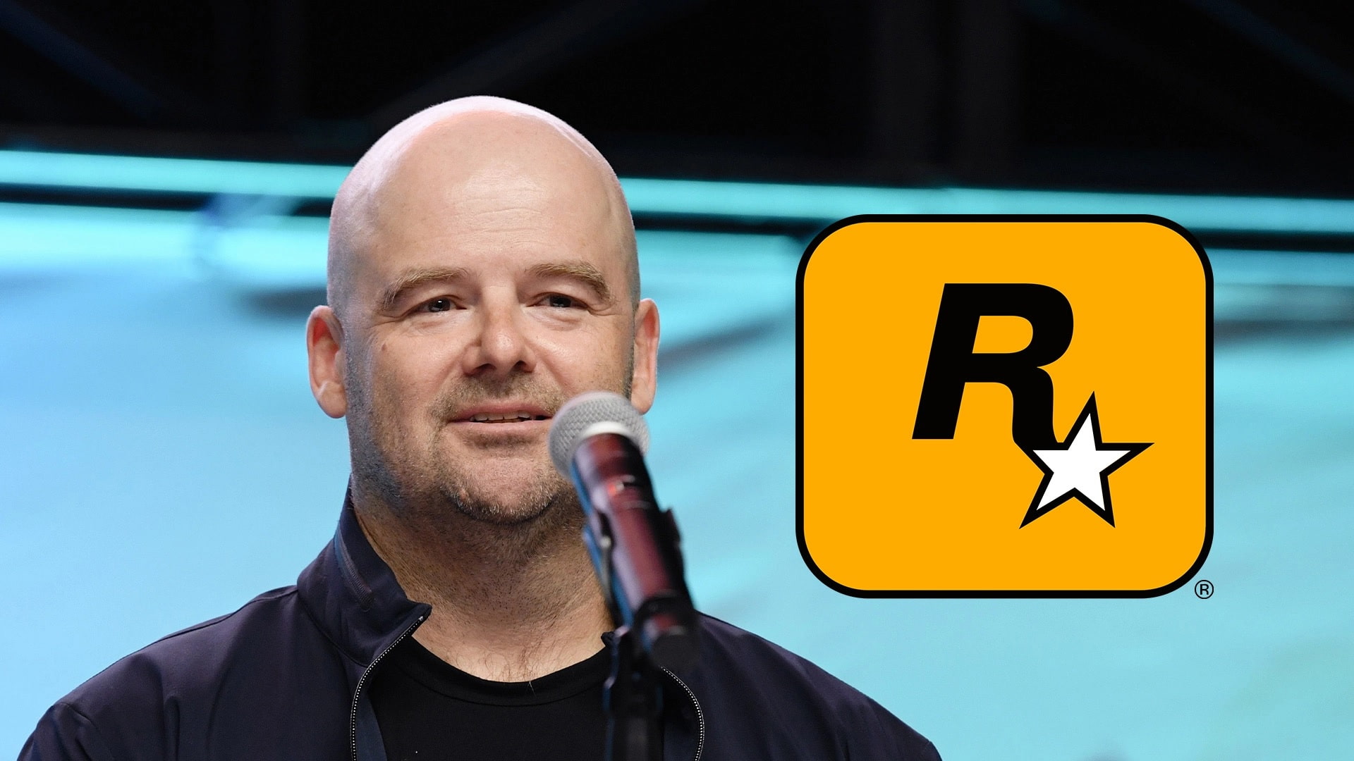 Rockstar Co founder Dan Houser Says Theres No Right Way to Play an Open world Game Speaker at a Microphone on Stage with a Large Yellow Rounded square Logo Showing a Black 'r' and White Star to the Right